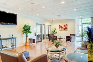 A hotel lobby with leather seating, a flat-screen TV, potted plants, and a large window.