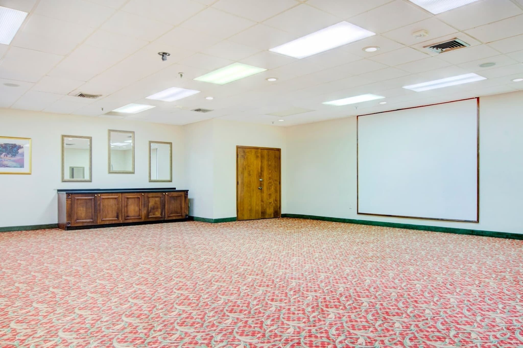 Une salle de conférence avec un tapis à motifs, un meuble en bois, une porte et un tableau blanc mural.