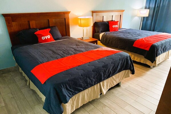 Deux lits doubles avec des têtes de lit assorties, une table de chevet avec une lampe et un oreiller rouge orné du mot « oyo ».