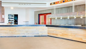 Zona de recepción con mostrador de madera, estación de café en la pared y una puerta roja.