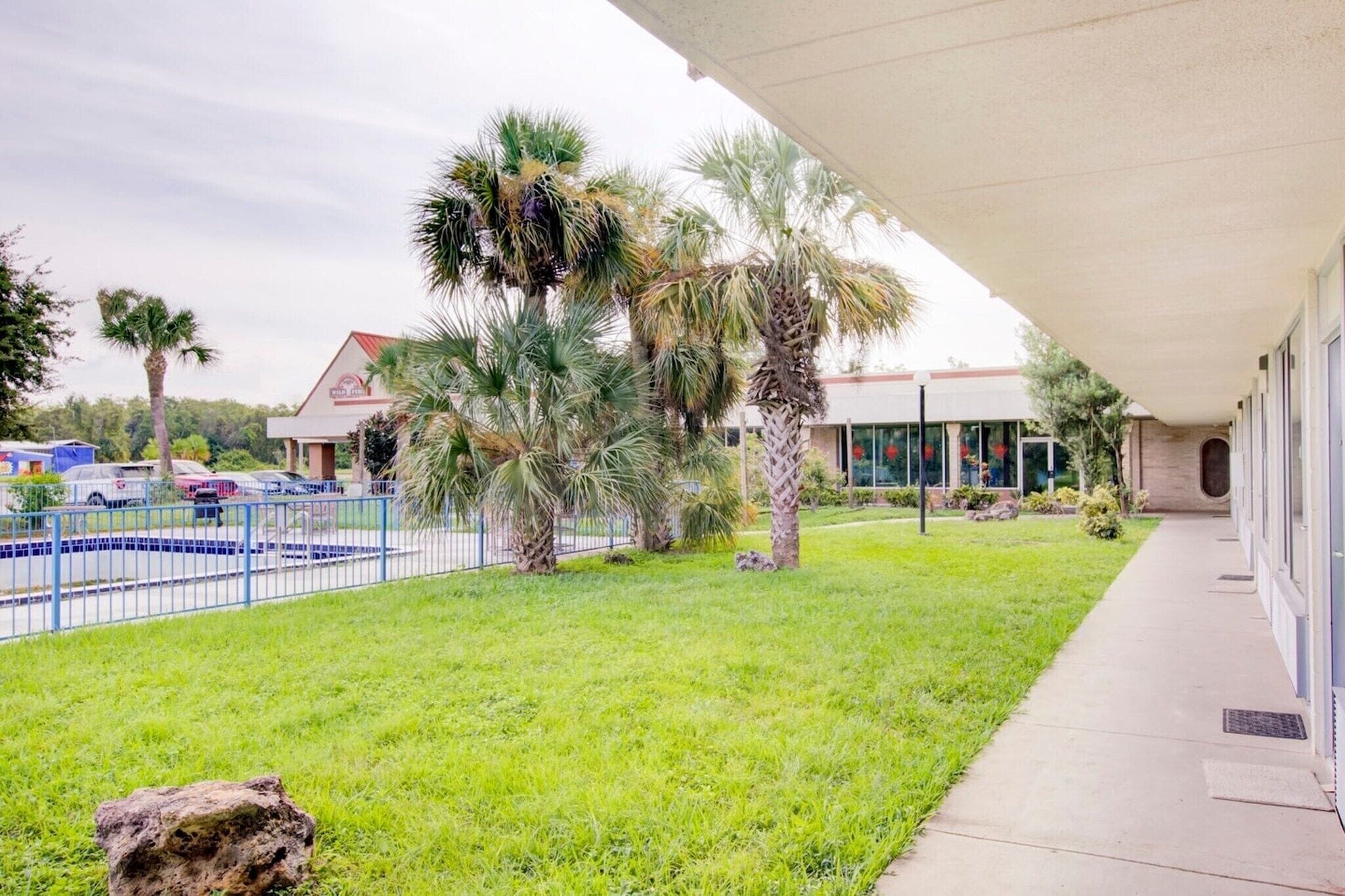 A building with a covered walkway, a swimming pool, and palm trees.