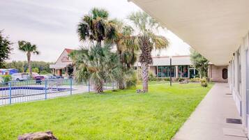A building with a covered walkway, a swimming pool, and palm trees.