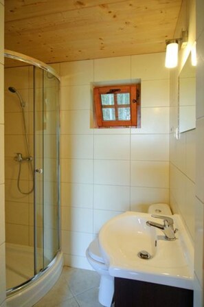 A bathroom with a glass shower enclosure, a white sink, and a small window above the toilet. - Summer Cottages in Kashubia (Bytow)