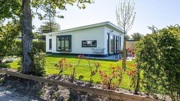 A modern single-story house with a covered patio, a lawn, and a wooden fence.
