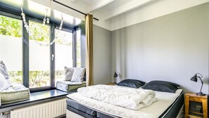 A bedroom with a bed, a window seat, a bedside table, and a radiator.