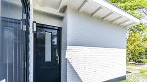 A modern building with a black door, white brick wall, and a paved area with grass patches.