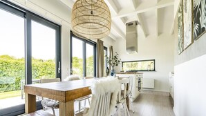 A modern kitchen with white cabinetry, a wooden dining table, and a large window overlooking greenery.