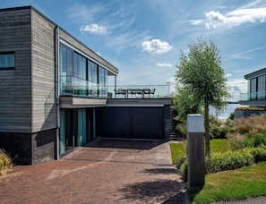 Ein modernes, zweistöckiges Haus mit einem Glasbalkon, einem Ziegelweg und Blick auf das Wasser.