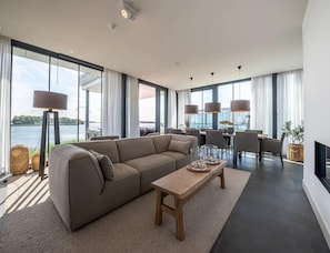 Ein modernes Wohnzimmer mit großem Fenster, einer Couch, einem Holztisch und einem Essbereich mit Stühlen und Tisch.