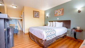 A hotel room with a bed, a desk, a chair, a refrigerator, and a wall with a map and a picture.