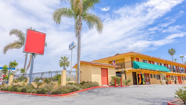 A motel with a yellow facade, a green awning, and a red signboard.