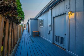 A narrow wooden deck leading to a building with a door and a small table.