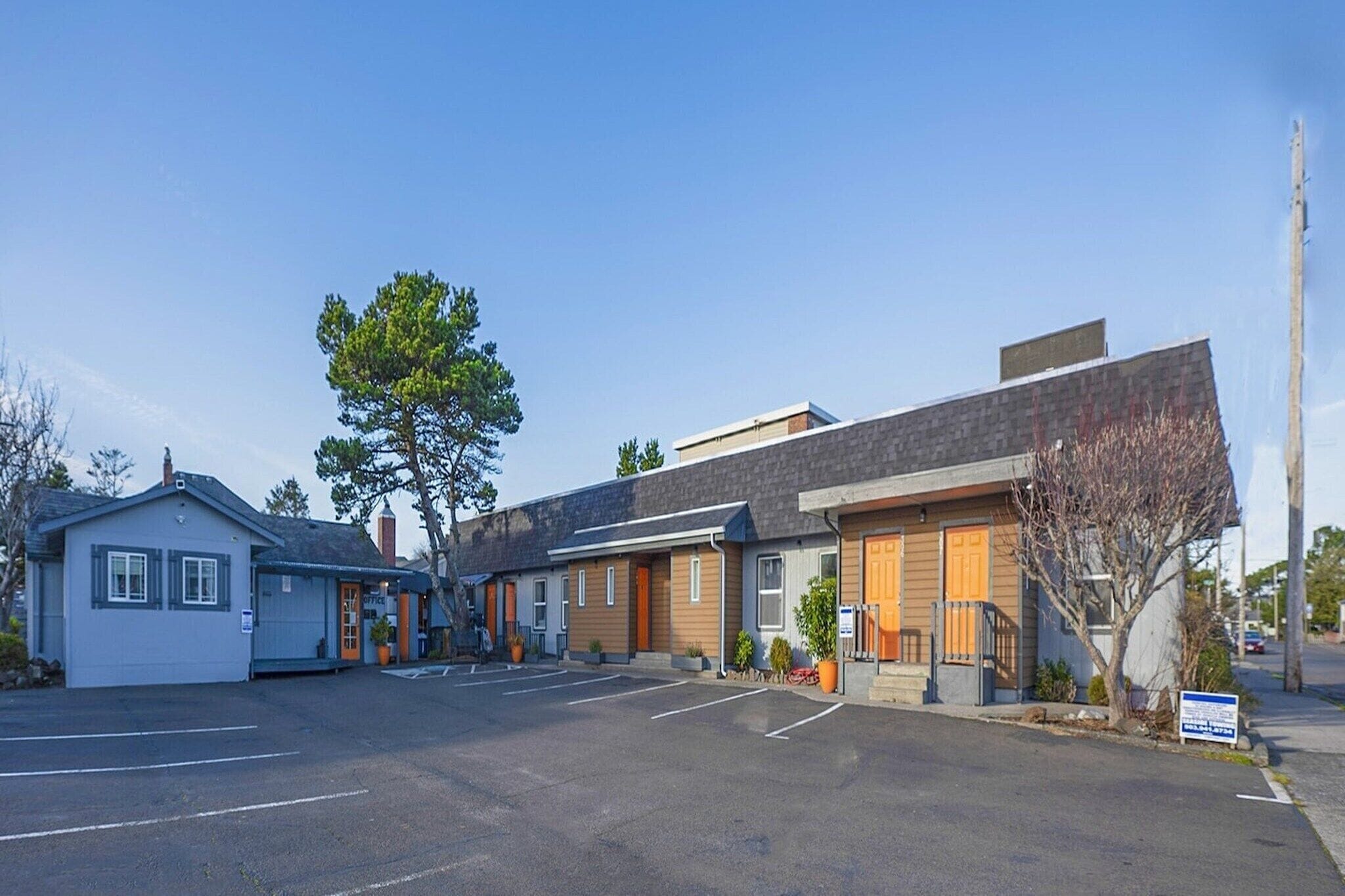 A motel with a parking lot, a small building, and a large building with a sloped roof.