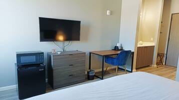 Habitación de hotel con una cama, un escritorio con silla, televisor, microondas y un pequeño cubo de basura.