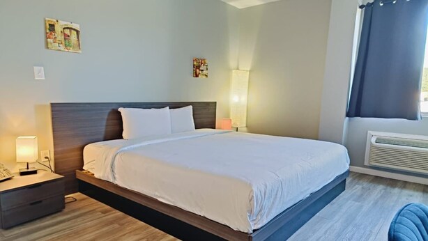 Una camera d'hotel con un letto, un comodino, una lampada, opere d'arte a parete e una finestra con tende.