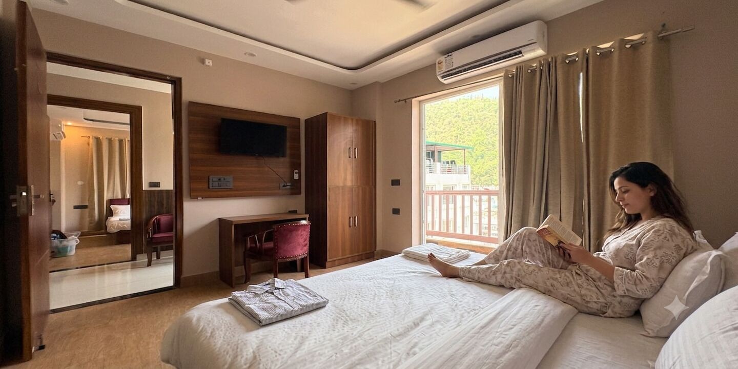 A bedroom with a bed, a desk, a chair, a TV, and a window with curtains.