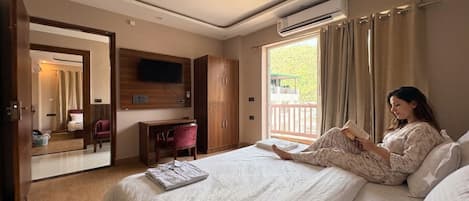 A bedroom with a bed, a desk, a chair, a TV, and a window with curtains.