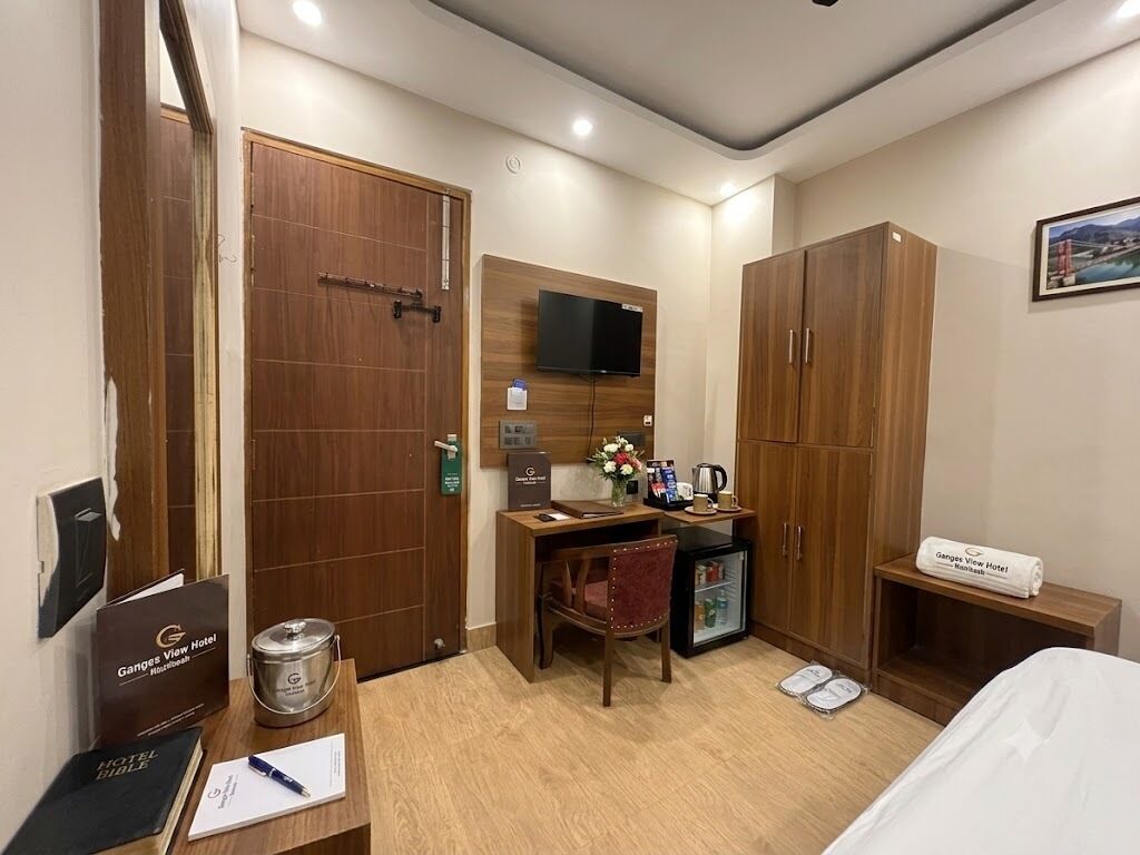 A hotel room with a wooden desk, a television, a minibar, a bed, and a framed picture on the wall.