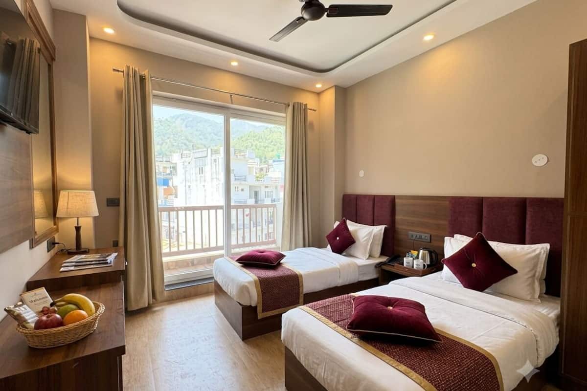 Habitación de hotel con dos camas, un escritorio con lámpara, ventana con cortinas y balcón.