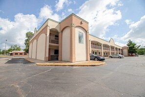 A building with a beige facade, multiple balconies, and a parking lot.