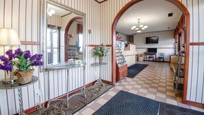 A hotel lobby with striped walls, a checkered floor, a mirror, a small table with flowers, and a television.