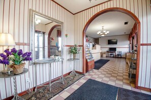 A hotel lobby with striped walls, a checkered floor, a mirror, a small table with flowers, and a television.