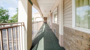 A covered corridor with a metal railing, a stone wall, and a window on the right.