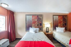 Habitación de hotel con dos camas, una ventana con cortinas, un aire acondicionado de pared y dos cuadros.