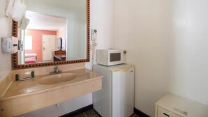 A bathroom with a sink, mirror, microwave, and a small cabinet.