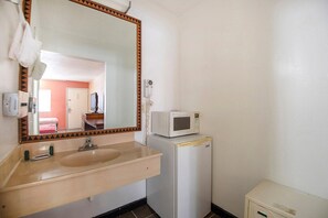 A bathroom with a sink, mirror, microwave, and a small cabinet.