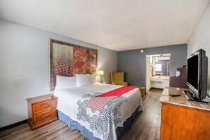 A hotel room with a bed, a nightstand, a TV, a mirror, and a door leading to a bathroom.