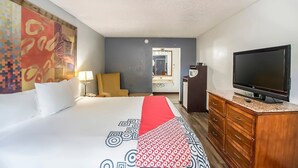 A hotel room with a bed, a TV, a wooden dresser, and a large painting on the wall.