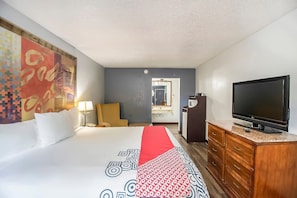 A hotel room with a bed, a TV, a wooden dresser, and a large painting on the wall.