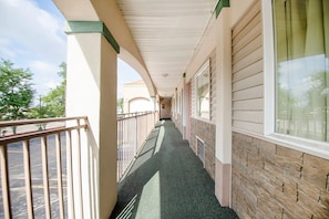 A covered corridor with a metal railing, a stone wall, and a window on the right.