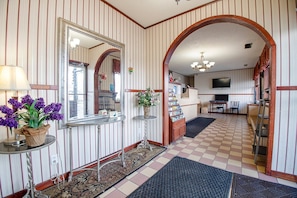 A hotel lobby with striped walls, a checkered floor, a mirror, a small table with flowers, and a television.