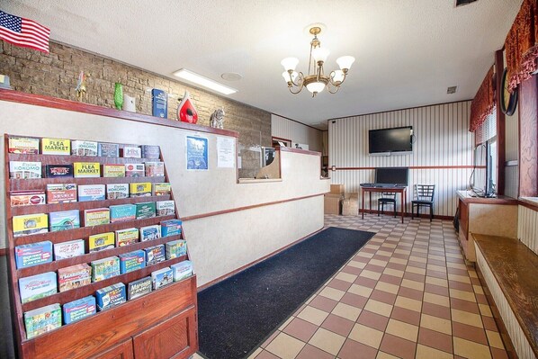 Un hall d’entrée avec un sol à carreaux, un comptoir d’accueil, un téléviseur fixé au mur et une étagère où sont exposés des livres.