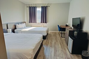 A hotel room with two beds, a desk with a television, and a small kitchenette.