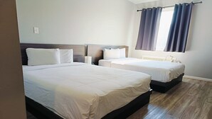 Ein Hotelzimmer mit zwei Betten, einem Fenster mit Vorhängen und Holzboden.