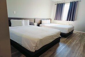 Una habitación de hotel con dos camas, un ventanal con cortinas y suelo de madera.