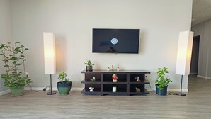 Ein Wohnzimmer mit an der Wand montiertem Fernseher, einer niedrigen Unterhaltungsecke aus dunklem Holz mit Regalen und zwei Stehlampen.