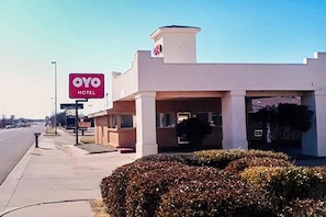 A hotel with a prominent red sign, a covered entrance, and a clear sky.