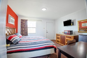 Una habitación de hotel con una cama, un escritorio, un televisor, un microondas y una puerta.