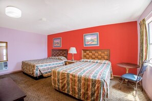 Ein Hotelzimmer mit zwei Betten, einem kleinen Tisch, einem Stuhl und einem Fenster mit Vorhängen.