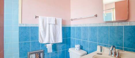 A bathroom with blue tiles, a white toilet, a sink, a mirror, and a towel rack.