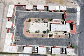 Vista aérea de um estacionamento com várias vagas, uma área central arborizada e edifícios adjacentes com telhados vermelhos.