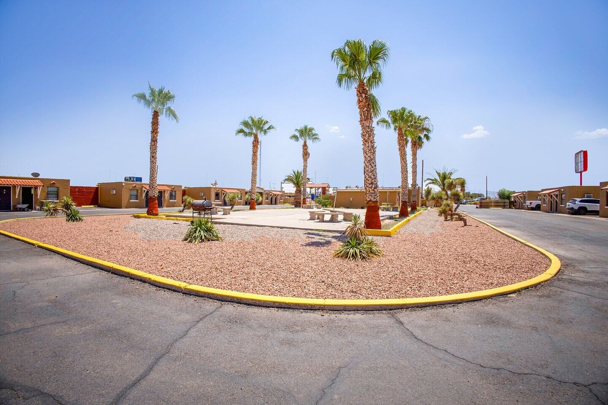 A parking lot with palm trees, a basketball court, and a building with a red sign.