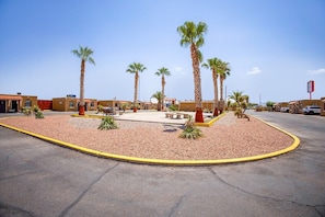 A parking lot with palm trees, a basketball court, and a building with a red sign.