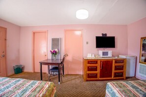 A room with two beds, a desk with a chair, a television, a microwave, and a small refrigerator.