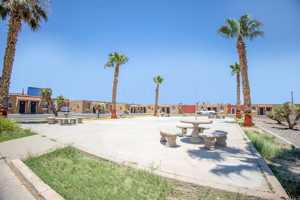 A courtyard with palm trees, outdoor seating, and a building with a red roof.