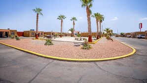 A parking lot with palm trees, a basketball court, and a building with a red sign. - King Bed Non-Smoking (El Paso TX)